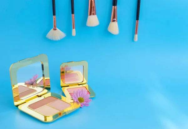 premium makeup brushes, palette eye shadow makeup and blush pads on a bright blue background, creative minimal cosmetics flat lay