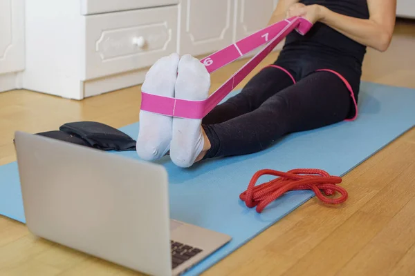 a girl gymnast trains with fitness resistance band at home via video connection on a laptop, remote sports