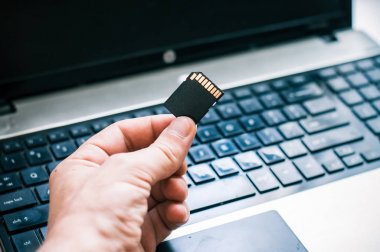 Sd bellek kartı ile bir dizüstü bilgisayar arka plan ofiste tutan el closeup.