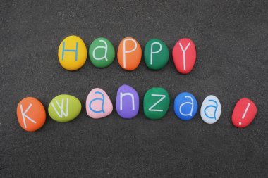 Happy Kwanzaa, African-American cultural celebration in the US lasting from 26 December to 1 January. Souvenir with multi colored and carved stone letters over black volcanic sand for a unique logo type clipart