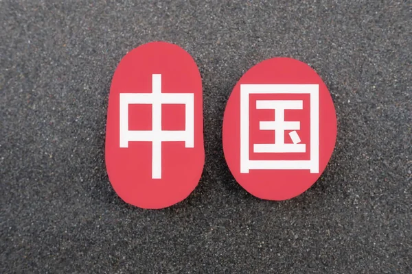 China country name in chinese simplified characters over two red stones and black volcanic sand background