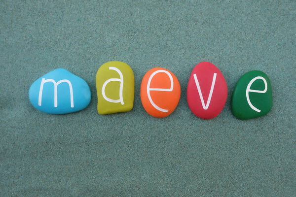 Maeve, женское имя ирландского происхождения, составленное из разноцветных каменных букв на зеленом песке
