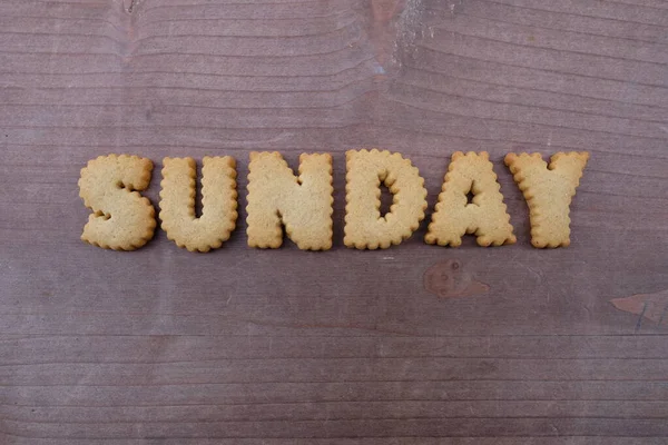 Sunday, the day of the week between Saturday and Monday composed with biscuit letters over a wooden board