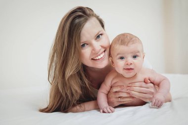 Yatak odasında yatağın üstünde onun bebek çocuk ile mutlu ve güzel genç anne