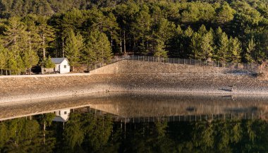 Küçük ev ve ağaçlar üzerinde baraj yansıyan