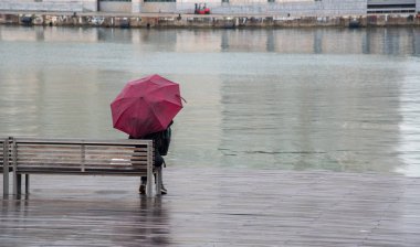 Genç kız ssitting yağmur altında ahşap bir bankta