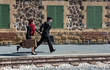 Klasik valizli genç çift tren istasyonunun dışında hızla koşuyor ve son trene yetişiyor.. 