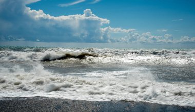 Fırtınalı gökyüzü ve dalgalı okyanus dalgaları kıyıya vuruyor.