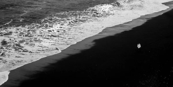 Persona no reconocida caminando en la playa de arena negra que ordena la —  Fotos de Stock