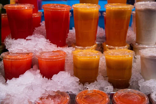Műanyag poharak kevert friss gyümölcslevekből jégen — Stock Fotó