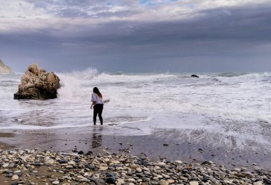 Tanımlanamayan kişi fırtınalı deniz manzarasının tadını çıkarıyor. Aphrodite Kayası, Kıbrıs 'ın Paphos bölgesinde Petra tou romiou kıyı şeridi
