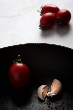 Kırmızı sağlıklı domates ve baharatlı sarımsak siyah bir mutfak tavasına izole edilmiş.