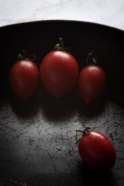 Siyah bir tavada izole edilmiş kırmızı sağlıklı domatesler.