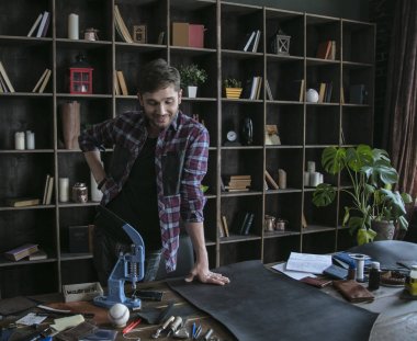 Erkek deri işçisi deri parçası ile ahşap masa yanında duruyor