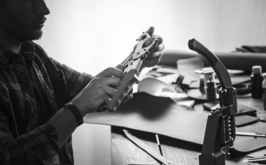 Genç adam deri üretici masanın arkasında oturuyor ve delik yumruk tutarak