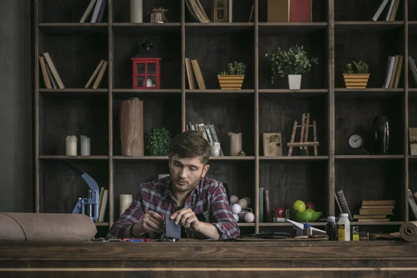Ahşap masa ve dikiş cüzdan arkasında deri üreticisi oturan genç adam