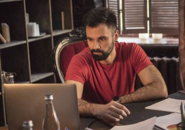 Genç iş adamı rahat karanlık ofiste dizüstü bilgisayar ile masada oturan sakallı