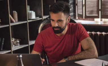 Sandalyede oturan ve masa üstünde laptop üzerinde sakallı genç işadamı