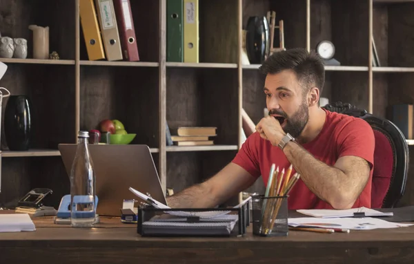 Studio dizüstü bilgisayar ile oturma ve şaşırtıcı haber tarafından şaşırtıcı genç işadamı