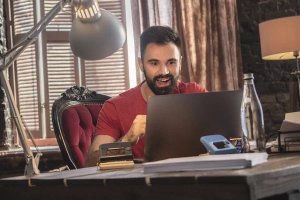 Dizüstü bilgisayar ile yumuşak sandalyede rahat ofisinde oturan genç işadamı