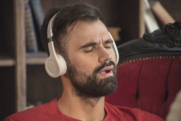Young bearded man in white headphones listening music with closed eyes