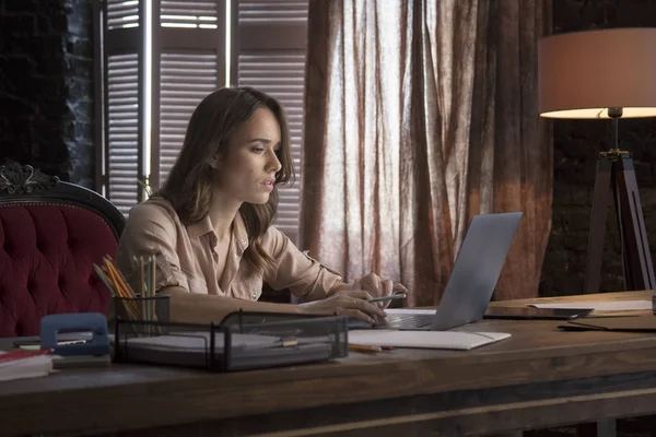 Young business woman sitting in office chair behind desk and working with laptop — Stock Photo, Image