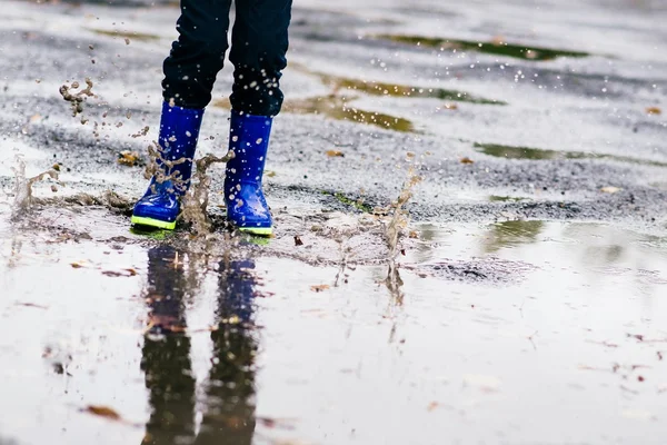Ragazzo in gomma blu stivali da pioggia che salta alla pozzanghera sporca — Foto Stock