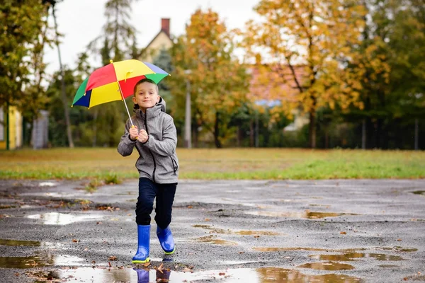 Boy in rubber blue rainboots jumping to dirty puddle — Stock Photo, Image