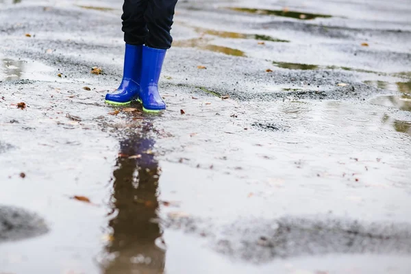 Ragazzo in gomma blu stivali da pioggia che salta alla pozzanghera sporca — Foto Stock