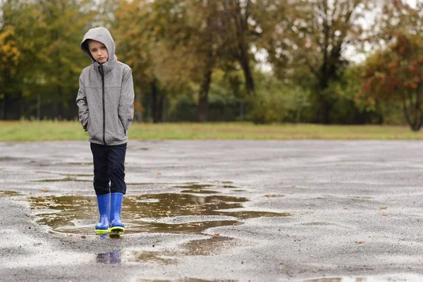 Ragazzo in gomma blu stivali da pioggia a piedi sotto la pioggia — Foto Stock