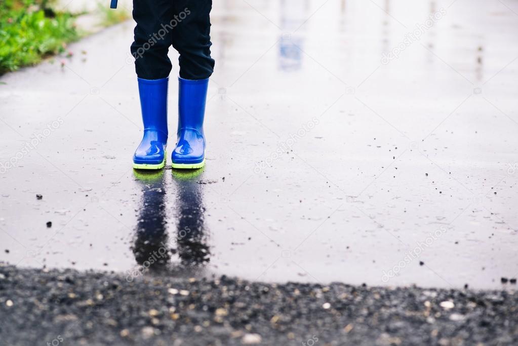 Child standing in rubber wellingtons on wet footpath.