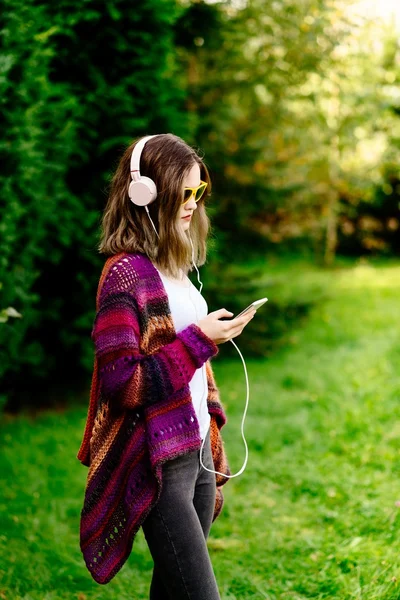 Woman in woolen sweater listening to music in park — Stock Photo, Image