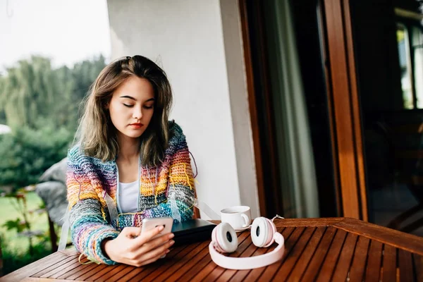 Mujer en suéter de lana utiliza un teléfono inteligente en la terraza . — Foto de Stock