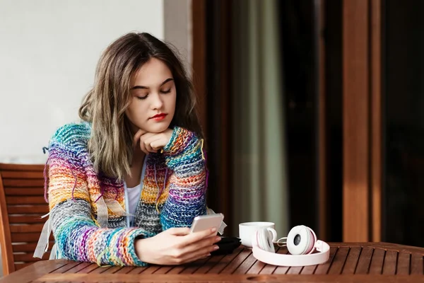 Mujer en suéter de lana utiliza un teléfono inteligente en la terraza . —  Fotos de Stock