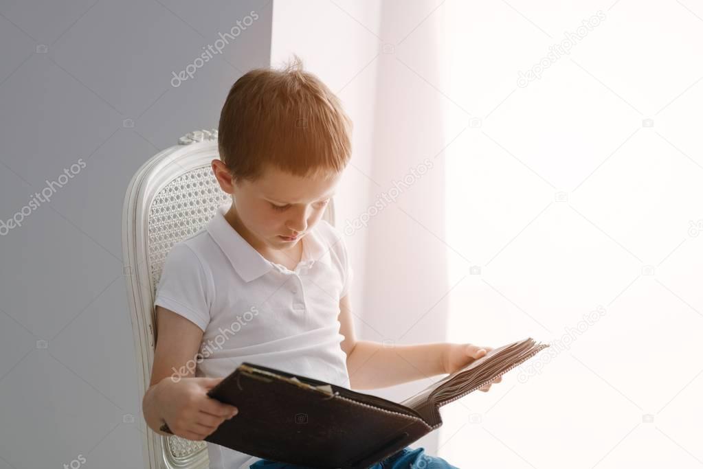 Little 7 years old boy browsing old photo album.