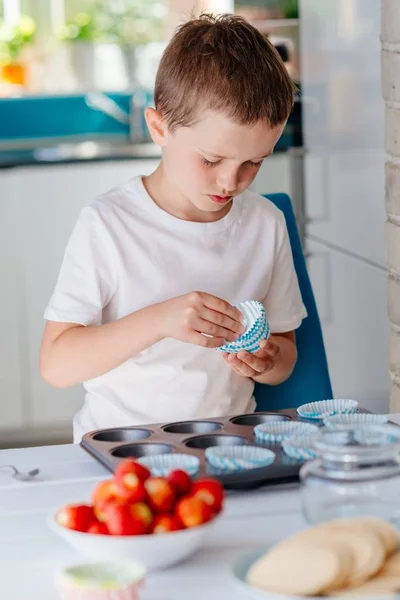 Niño colocando formas de magdalena en bandeja para hornear — Foto de Stock