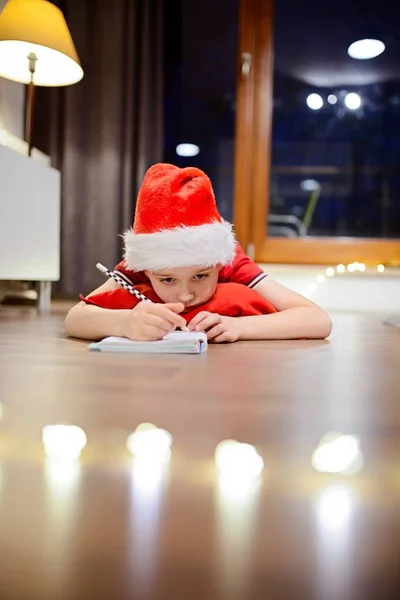 Συλλογισμένος μικρό αγόρι γράφει ένα γράμμα στον Άγιο Βασίλη — Φωτογραφία Αρχείου