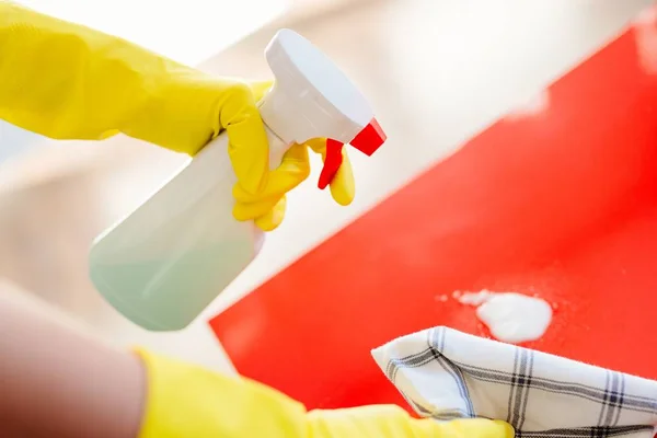 Mulher limpeza mesa vermelha com detergente spray e pano — Fotografia de Stock