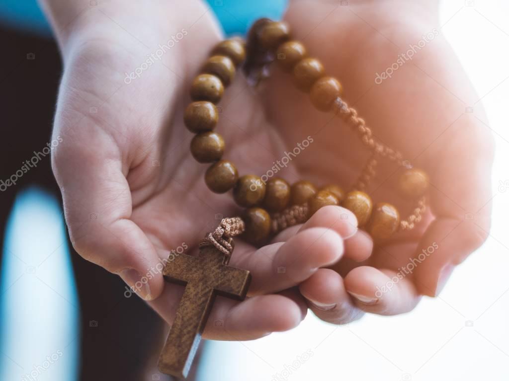 Little boy child praying and holding wooden rosary.