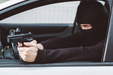 Siyah kar maskeli, silahlı bir adam araba kullanıyor..