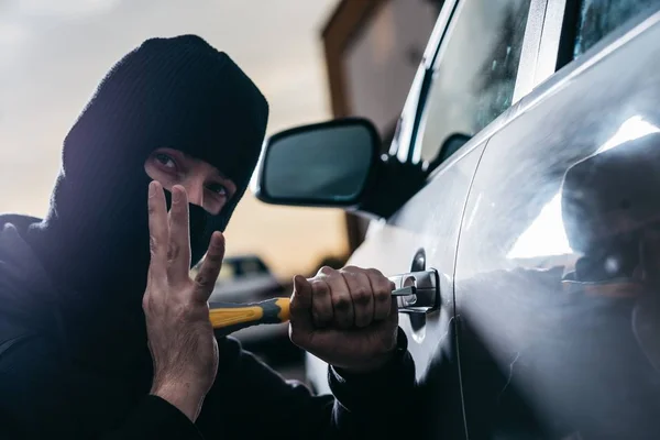 Ladrón de automóviles en pasamontañas negro tratando de entrar en el coche —  Fotos de Stock