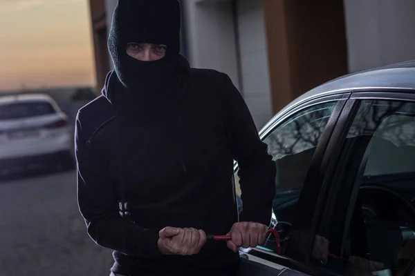 Ladrão de automóveis em balaclava preta tentando invadir o carro — Fotografia de Stock