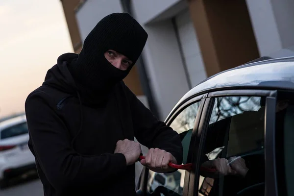 Ladrón de automóviles en pasamontañas negro tratando de entrar en el coche —  Fotos de Stock