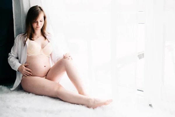 Femme enceinte en chemise blanche et lingerie assise — Photo