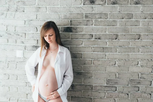 Vacker ung gravid kvinna poserar vid tegelväggen — Stockfoto