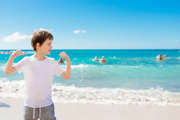 Heureux 7 ans garçon dans victoire succès geste sur la plage . — Photo