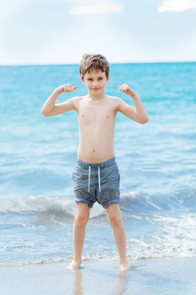 Feliz niño de 7 años en el gesto de éxito victoria en la playa . — Foto de Stock