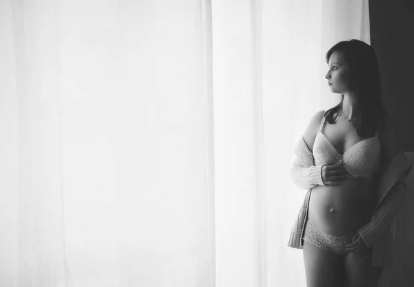 Donna incinta in piedi davanti alla finestra in soggiorno — Foto Stock