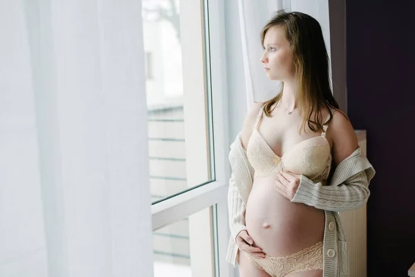 Donna incinta in piedi davanti alla finestra in soggiorno — Foto Stock