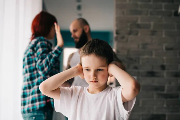 Verdrietig kind die betrekking hebben op zijn oren met handen tijdens ouders ruzie. — Stockfoto